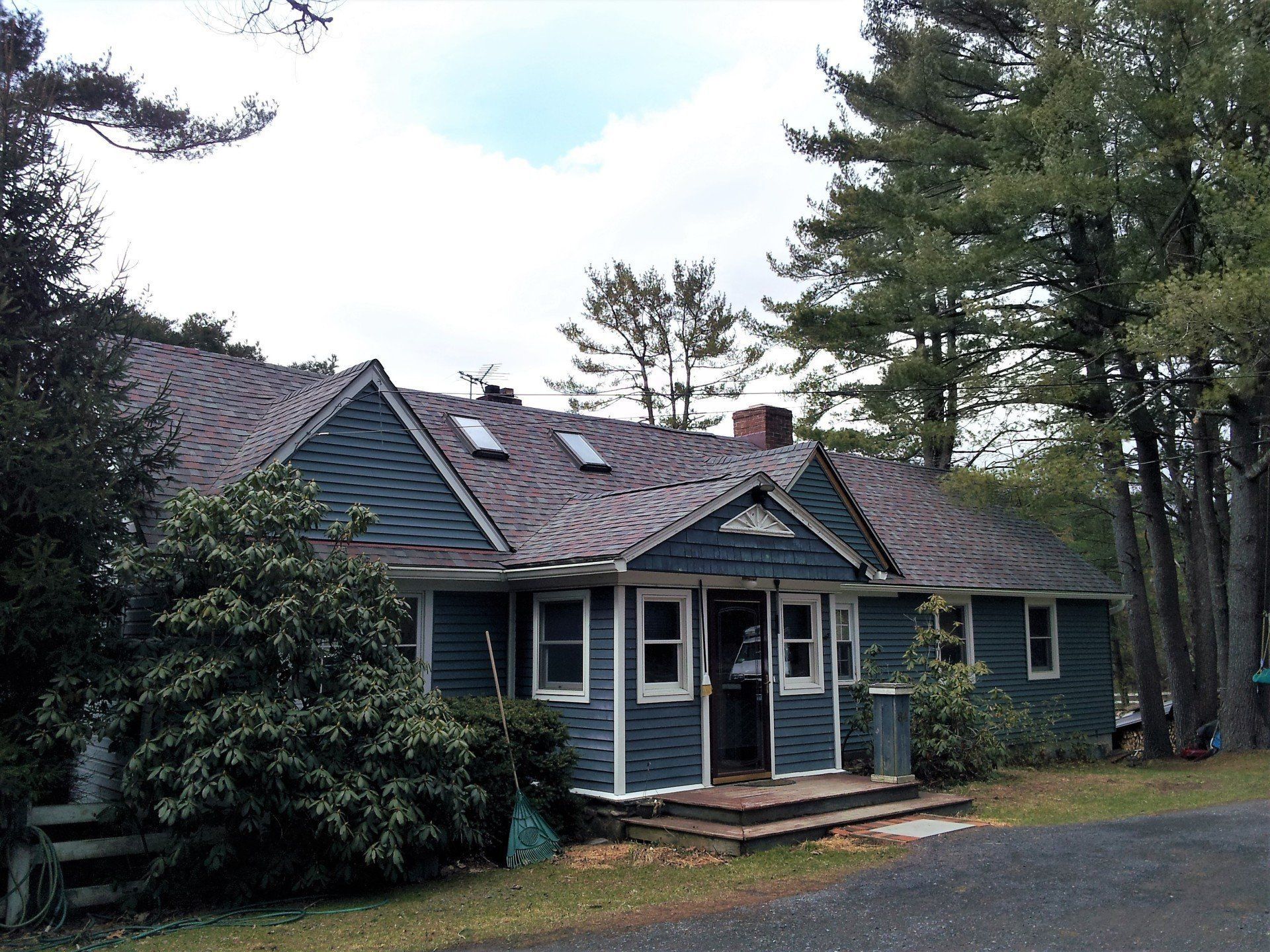 A blue house with a gray roof is surrounded by trees
