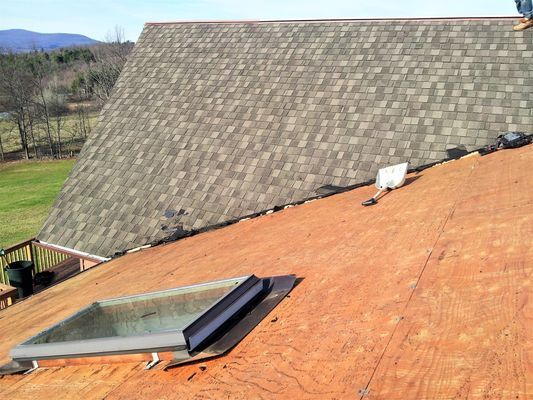 A man is standing on top of a roof with a skylight.