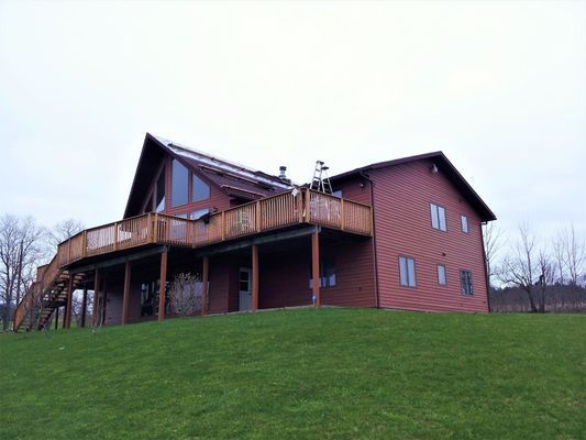 A large house with a large deck is sitting on top of a grassy hill.