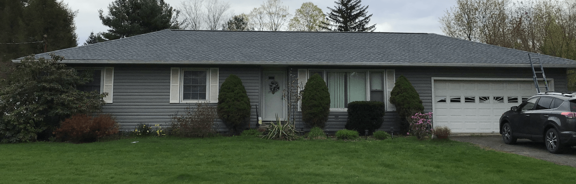 A gray house with a blue roof and a car parked in front of it.