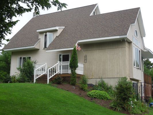 A large white house with a brown roof is sitting on top of a lush green hillside.