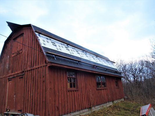 A red barn with a black roof and a ladder in front of it