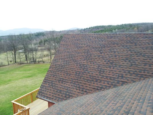 The roof of a house with a view of a field and trees.