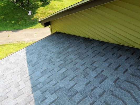 The roof of a house with a gray shingle roof and a yellow siding.