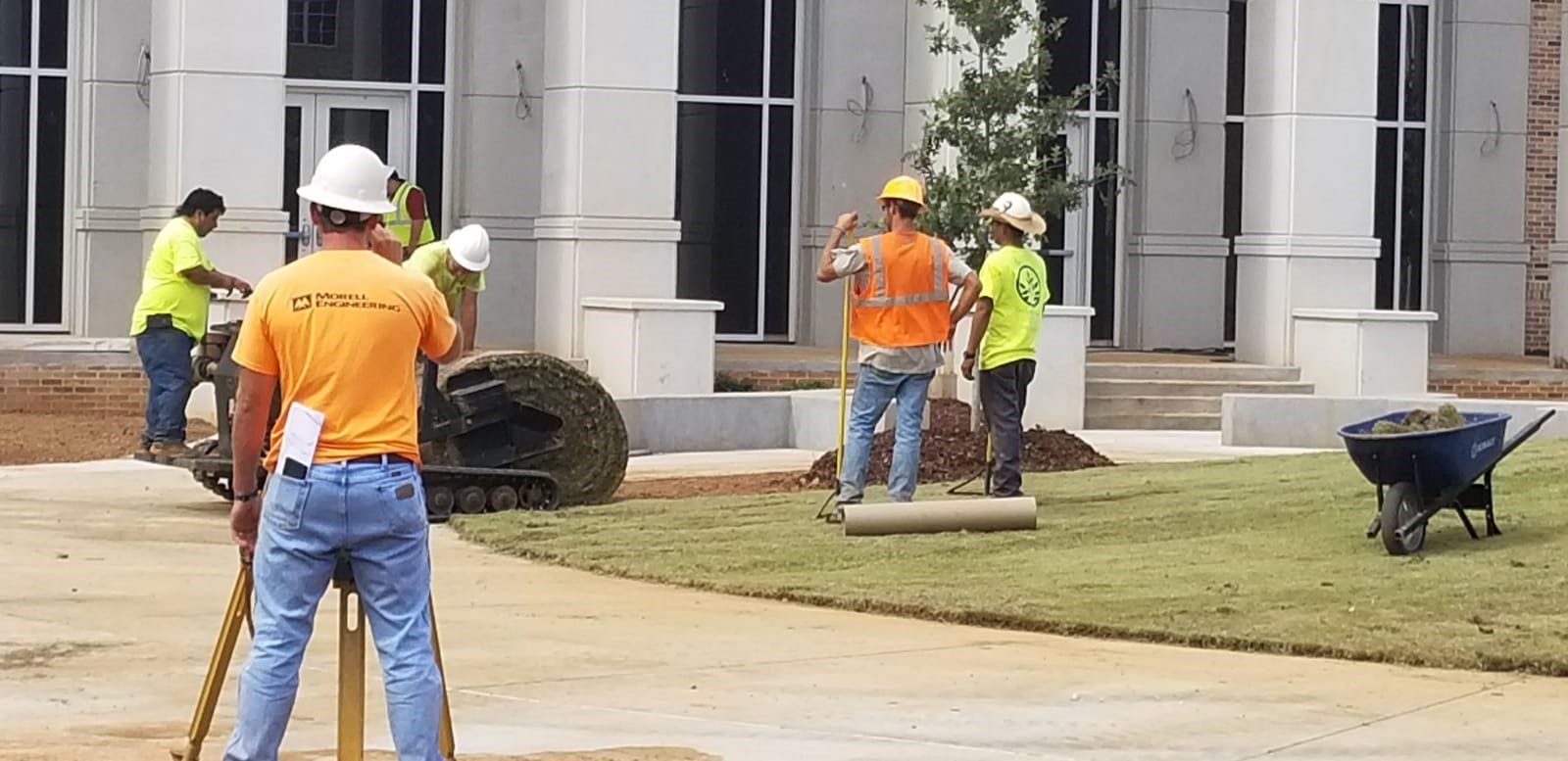 A group of construction workers are working on a lawn in front of a building.