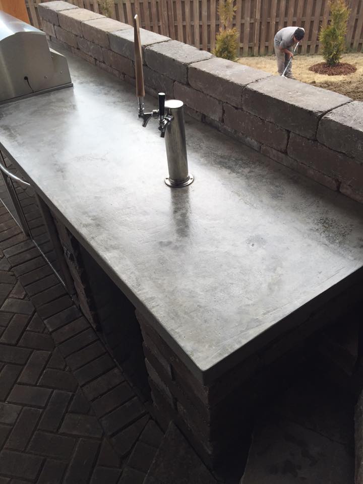 A concrete counter top with a faucet and a man standing behind it.