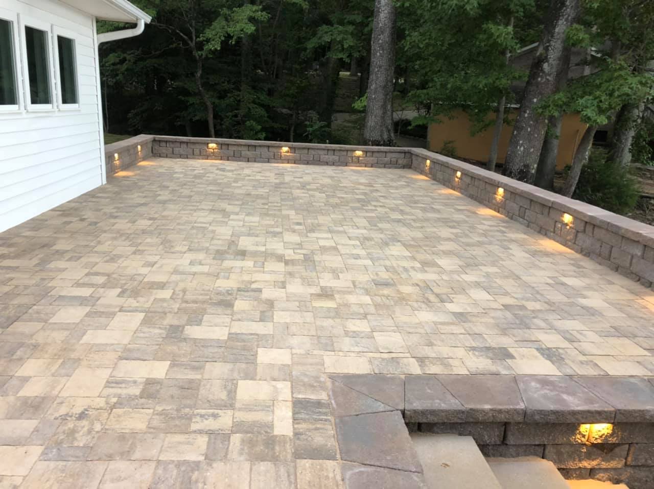A large brick patio with stairs leading up to it and trees in the background.