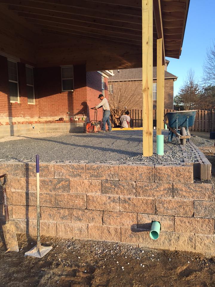 A man is working on a patio under a covered porch.