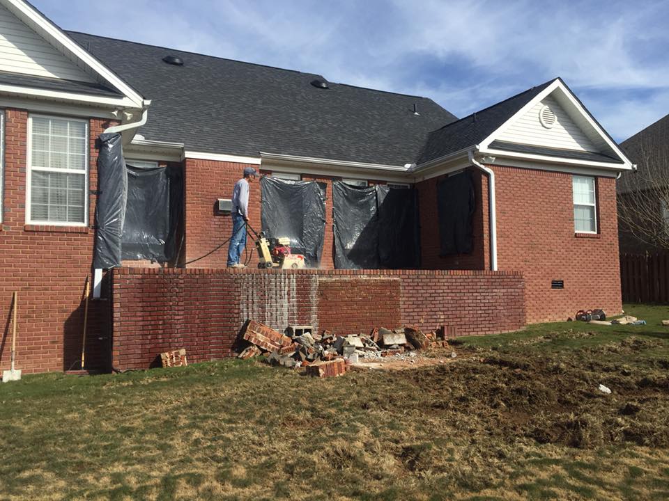 A man is standing on a porch of a brick house.