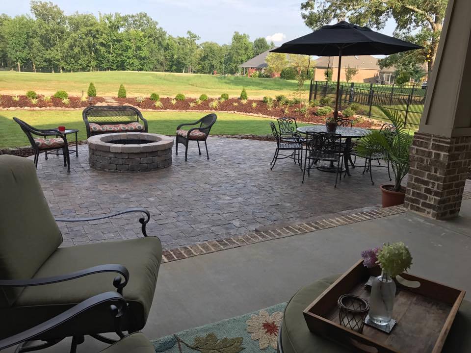 A patio with a fire pit , chairs , tables and umbrellas.