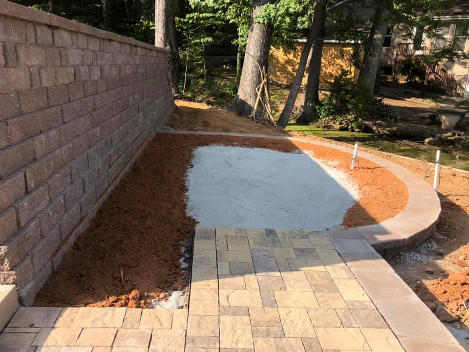 A brick wall and a brick walkway are being built in a backyard.