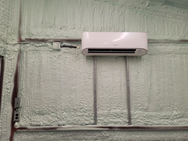 A white air conditioner is mounted on a wall covered in foam.