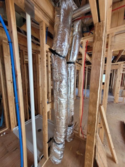 A building under construction with ducts hanging from the ceiling.