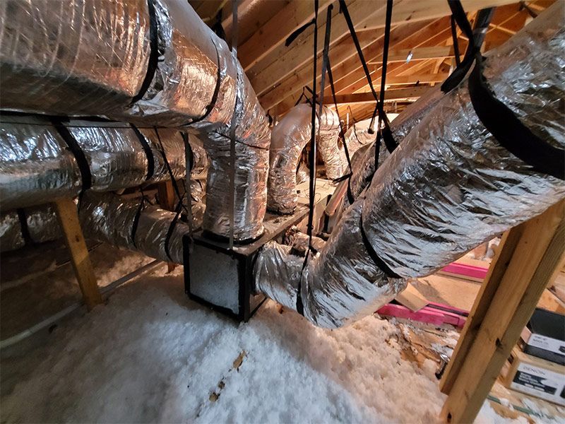 A bunch of ducts are hanging from the ceiling of an attic.