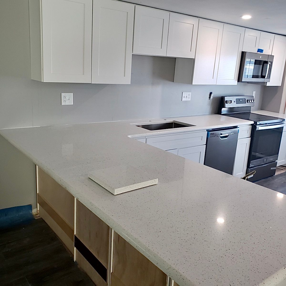 A kitchen with white cabinets , white counter tops , a stove and a microwave.