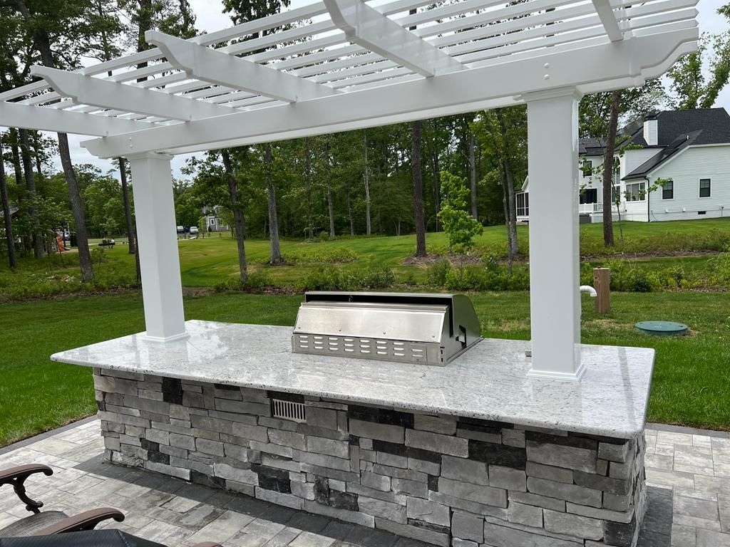 There is a grill under a pergola in the backyard.