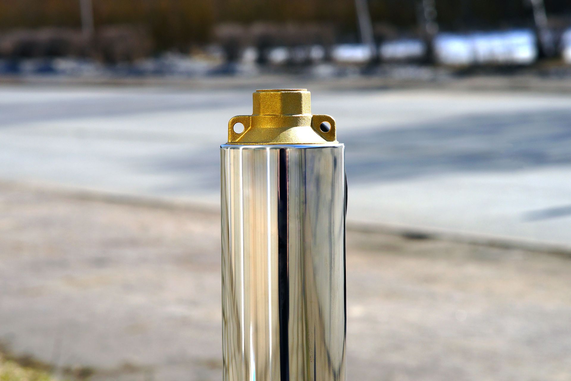 A close-up of a stainless steel submersible borehole pump with a brass discharge head, standing outdoors.