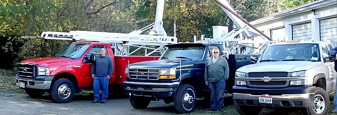 Three parked pickup trucks in front of a large structure, with two people standing beside them