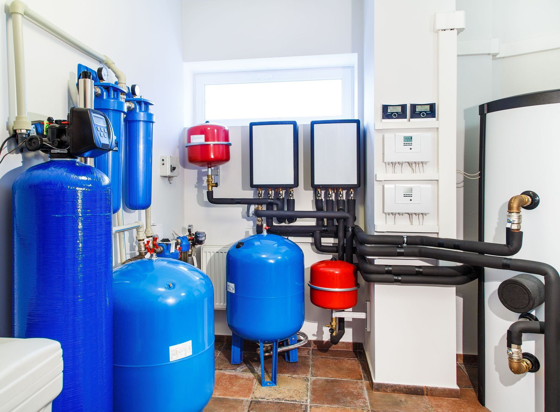 Residential utility room featuring a complex system of blue water tanks, red expansion vessels, and wall-mounted controls.