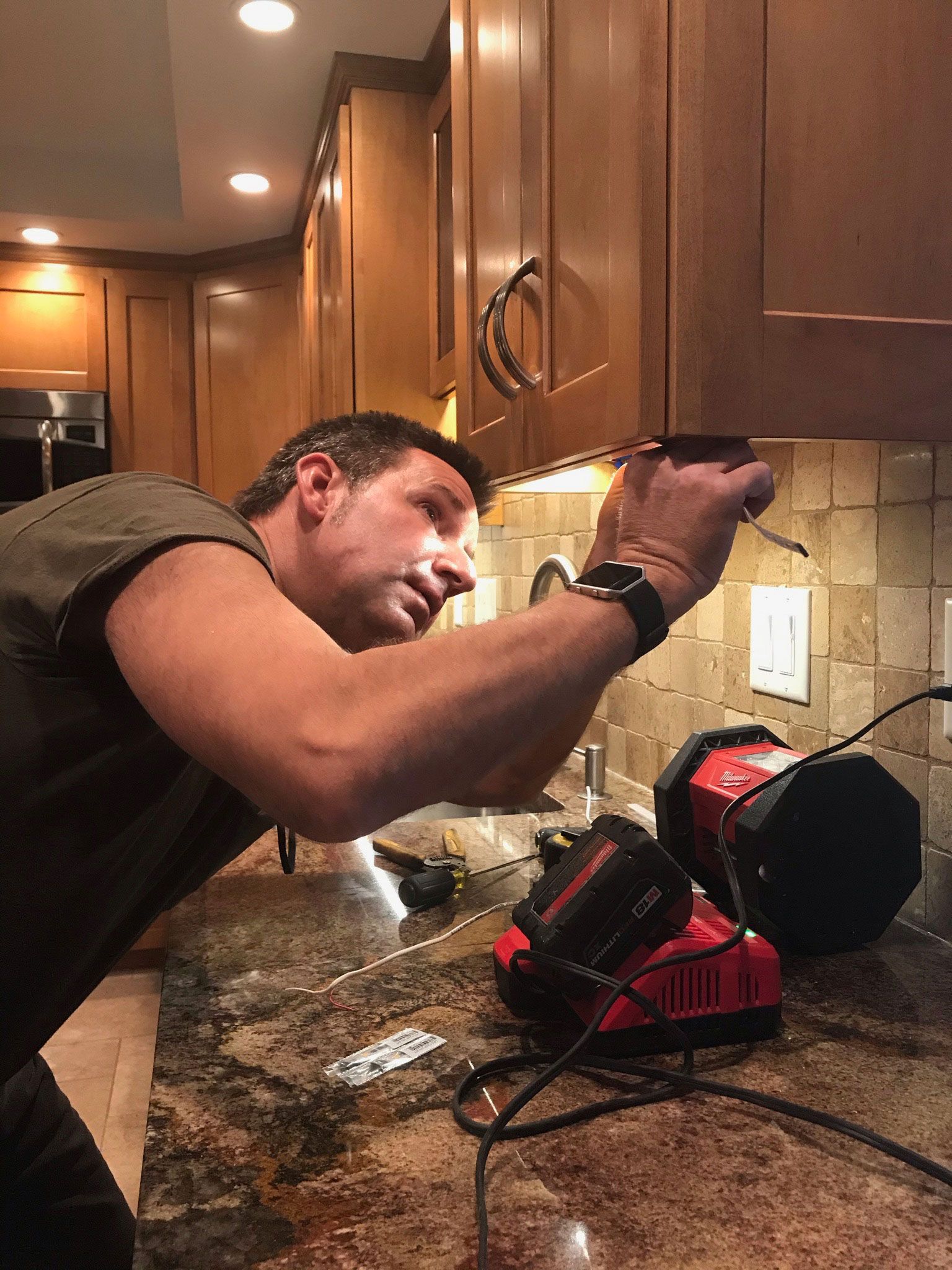 Man in a kitchen repairing a red appliance under cabinet lighting