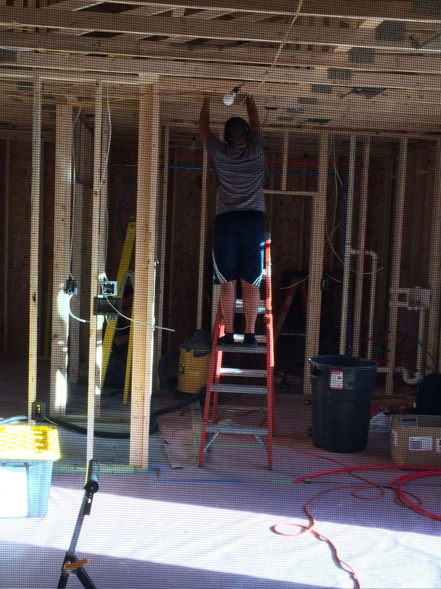 Person standing on a ladder in an unfinished room with exposed wooden studs and construction tools