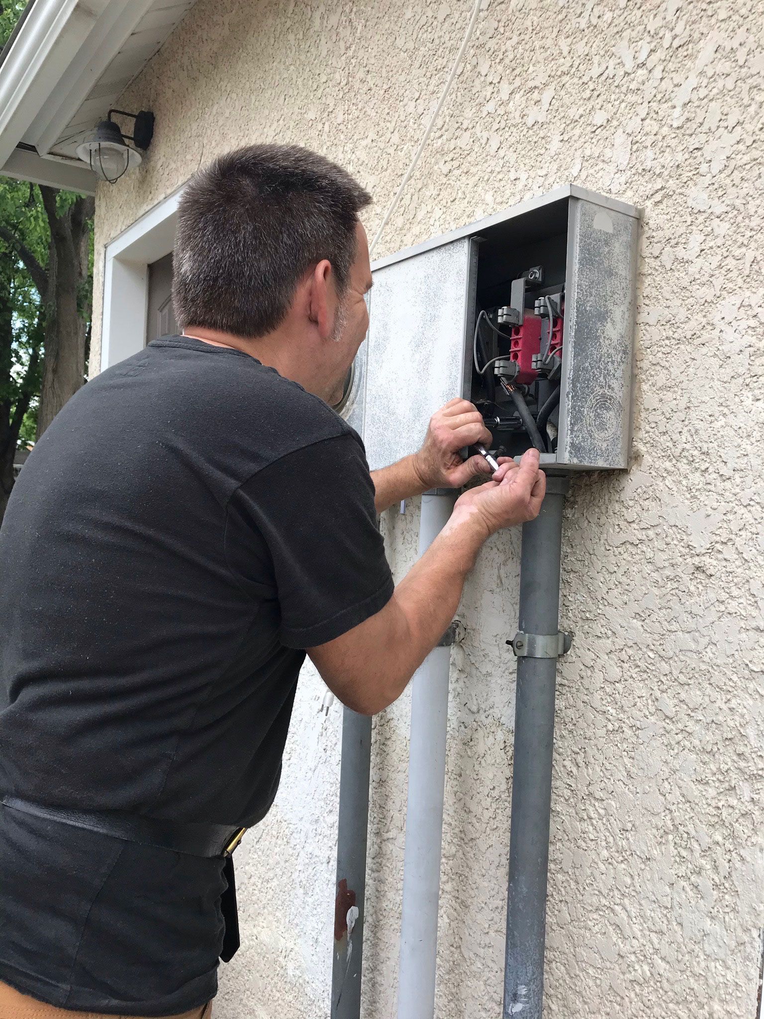 Technician repairing an open electrical panel mounted on an exterior wall.