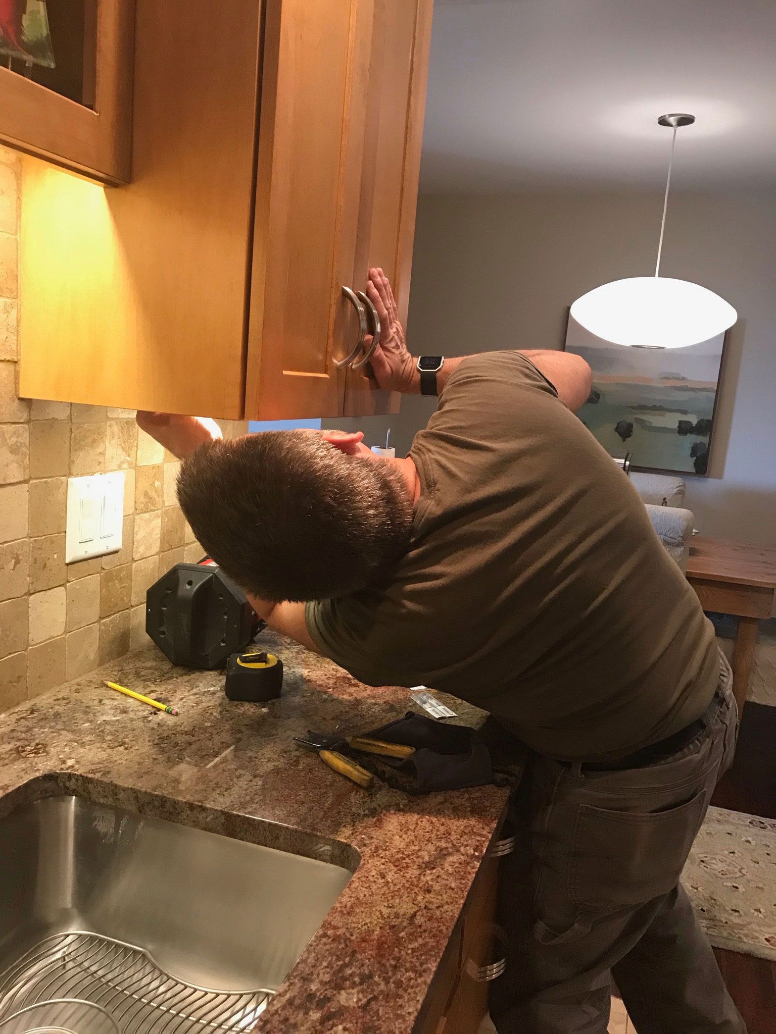 Person reaching up inside a kitchen cabinet over a granite counter and sink.