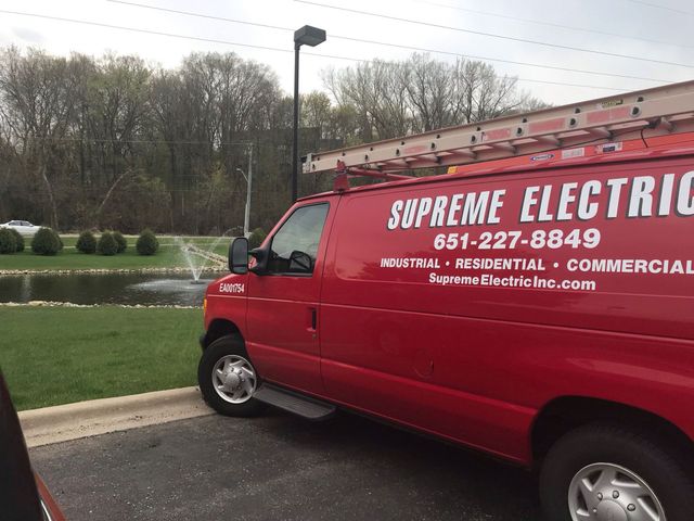 Red Supreme Electric service van parked by a grassy roadside, with business logo and phone number on the side