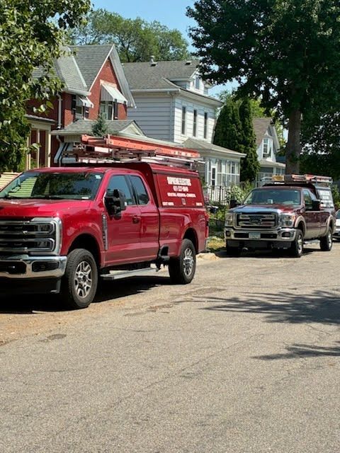 Red utility truck parked on a residential street beside another truck and houses.
