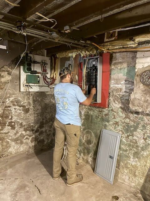 Person inspecting an electrical panel in a basement with exposed pipes and stone walls