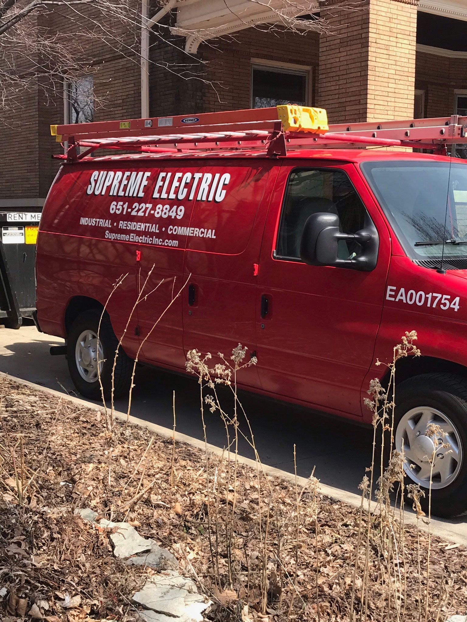 Red service van parked under a brick building, with leaf litter in the foreground.