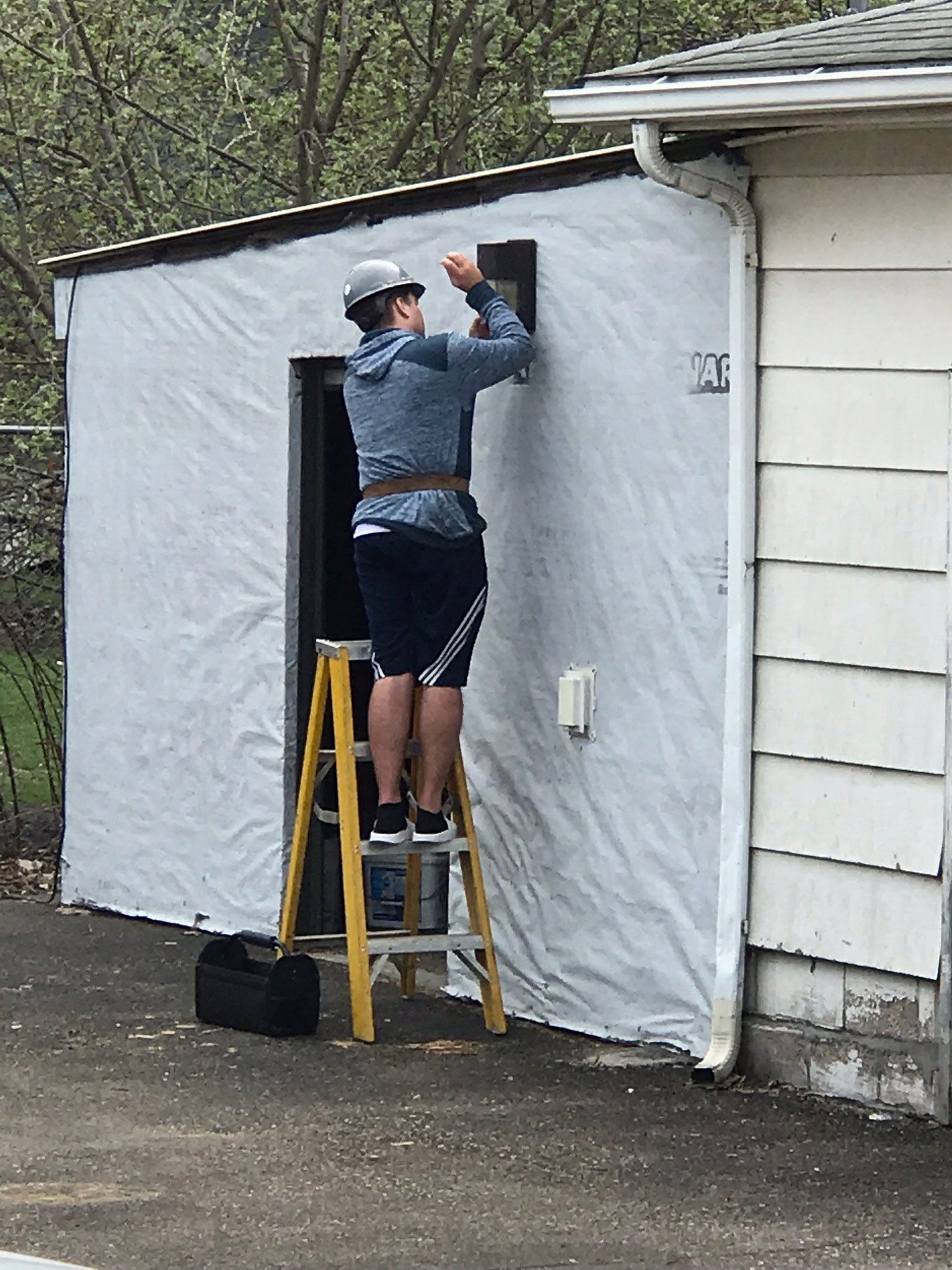 Person on a ladder installing white siding on a small building exterior