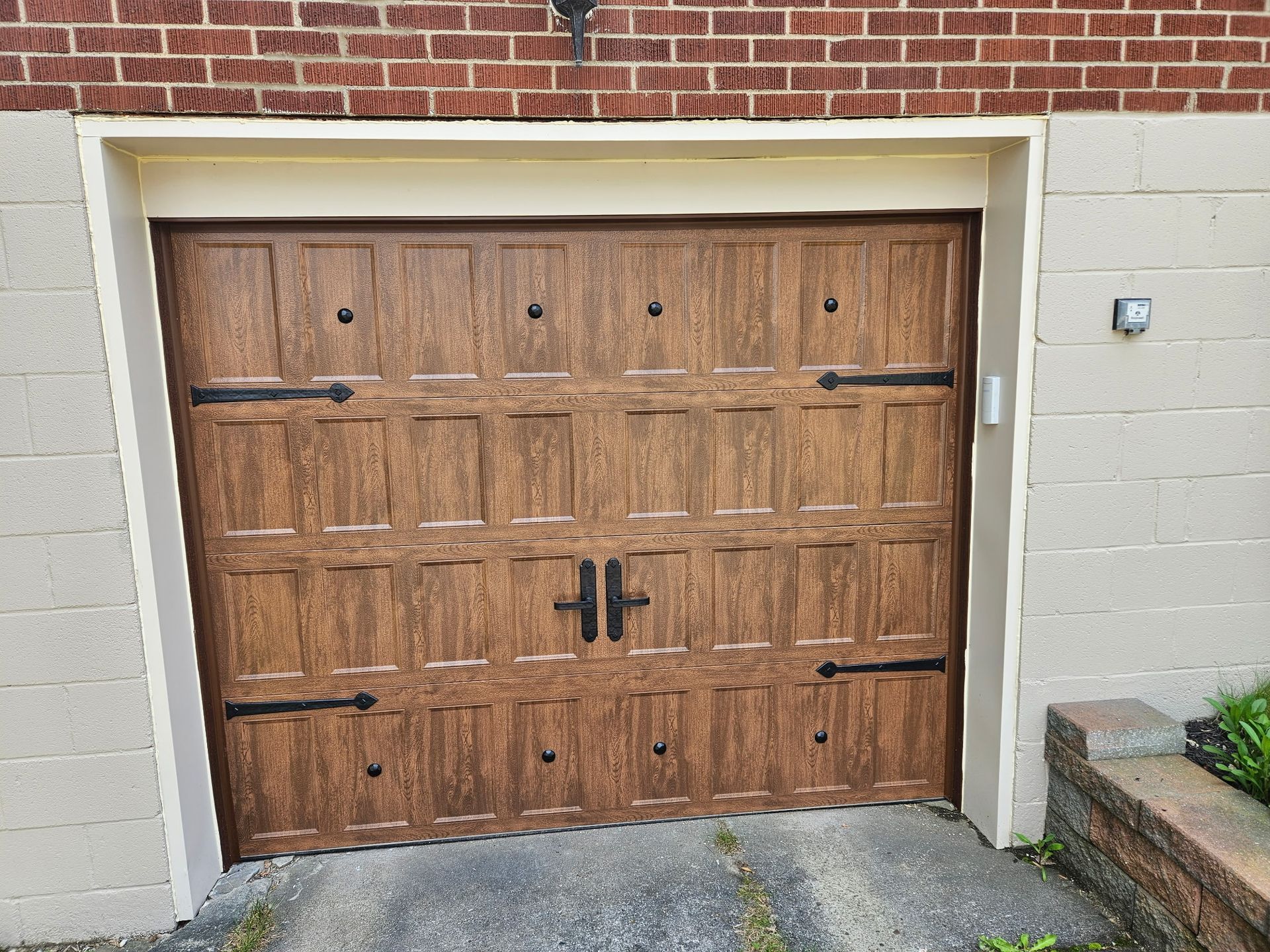Brown wooden garage door with black hardware, brick and concrete exterior.