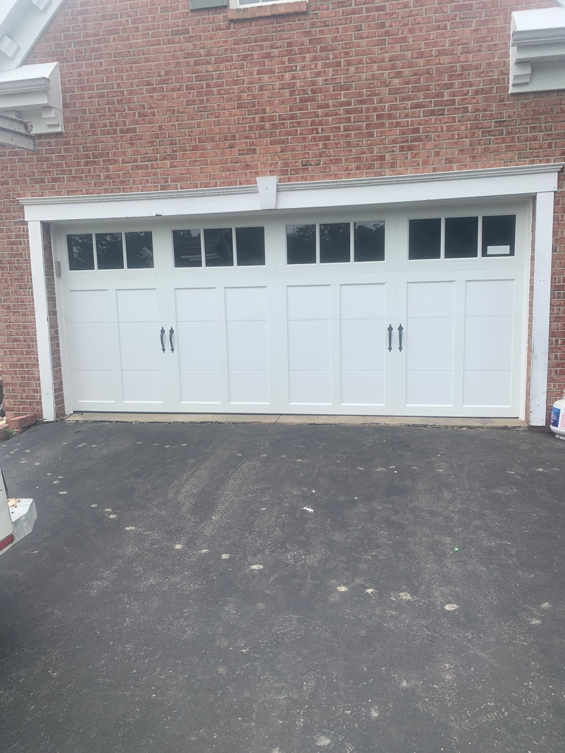 White garage door with windows, on a brick building with a black asphalt driveway.