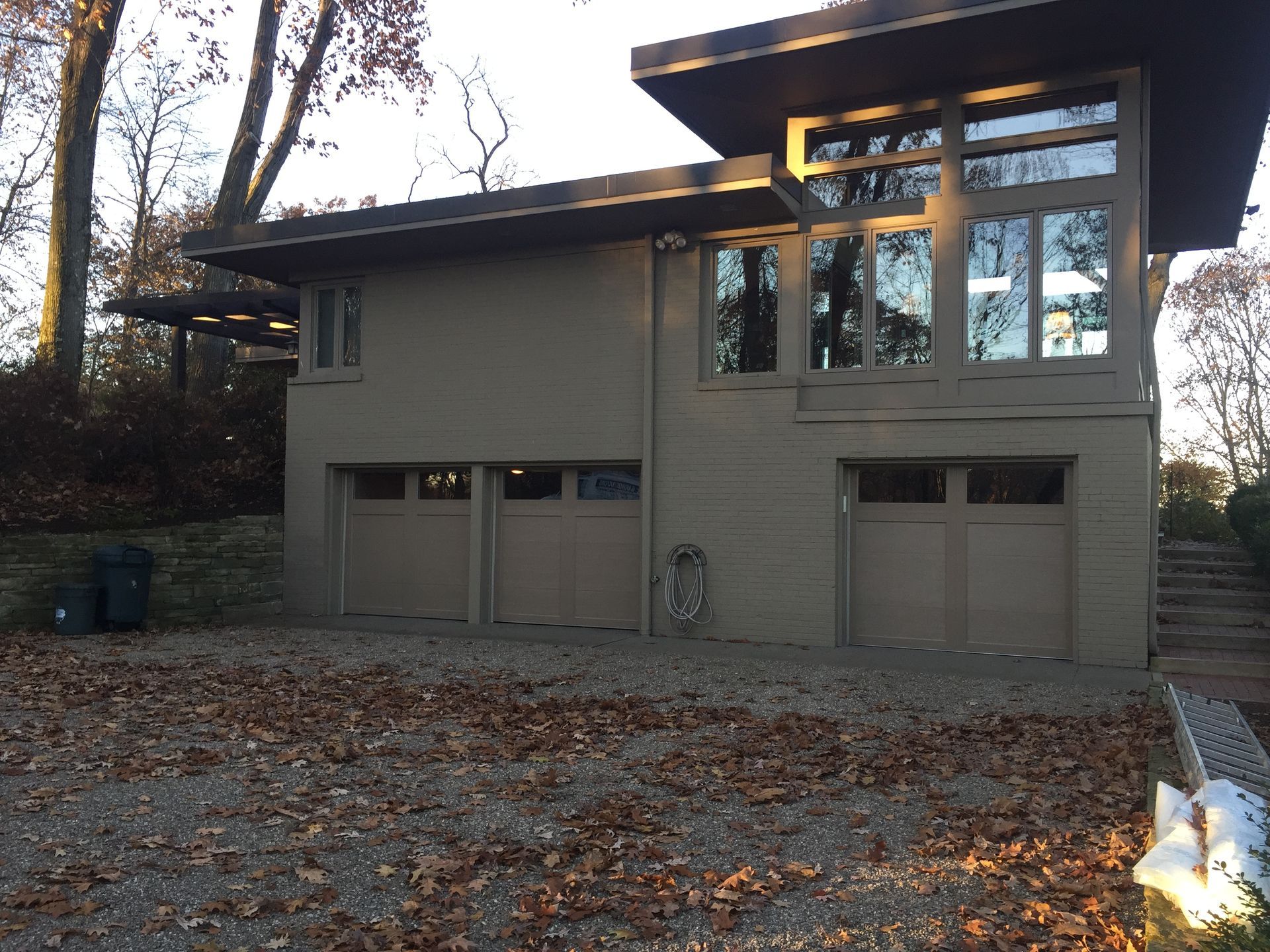 Three-car garage with brown doors, stone facade, and green metal roof on a concrete driveway.