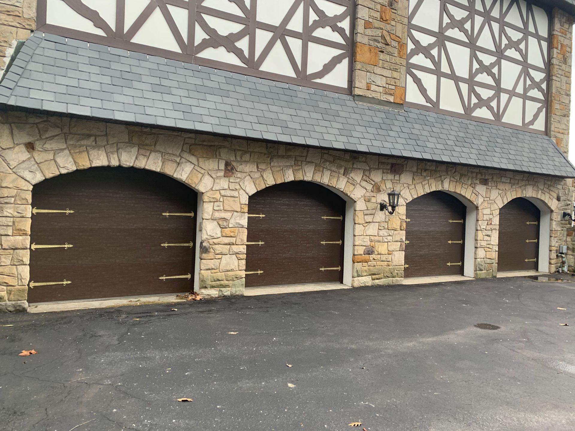 Exterior of a building with four arched, dark brown garage doors with stone facade and a gray roof.