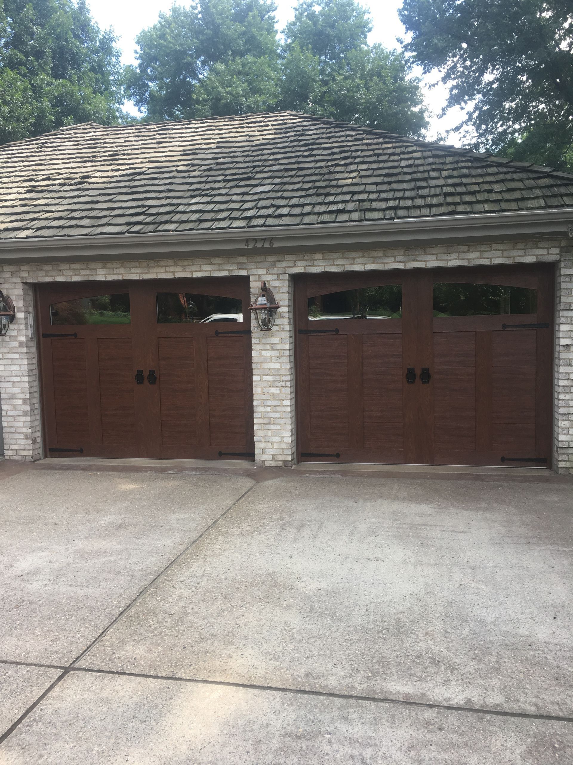 Brown garage doors in front of a concrete driveway and brick building with stone roof.