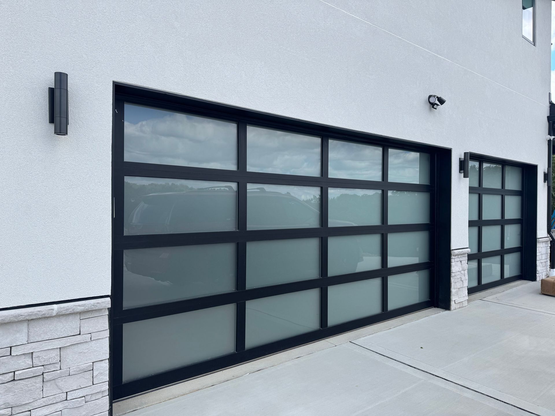 Modern garage doors with frosted glass panels and black frames on a white stucco building.