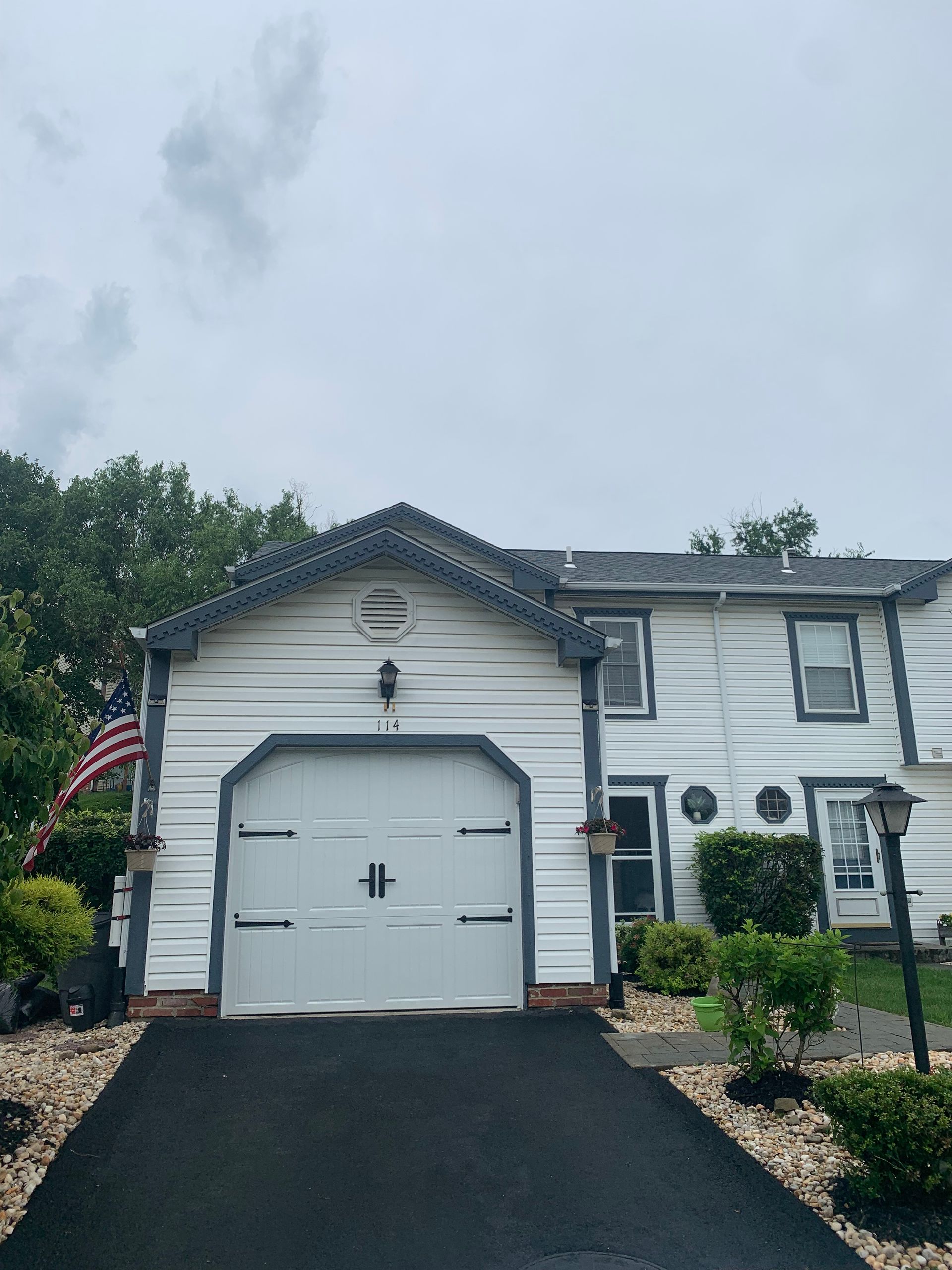 White townhome with attached garage, blue trim, and American flag on cloudy day.