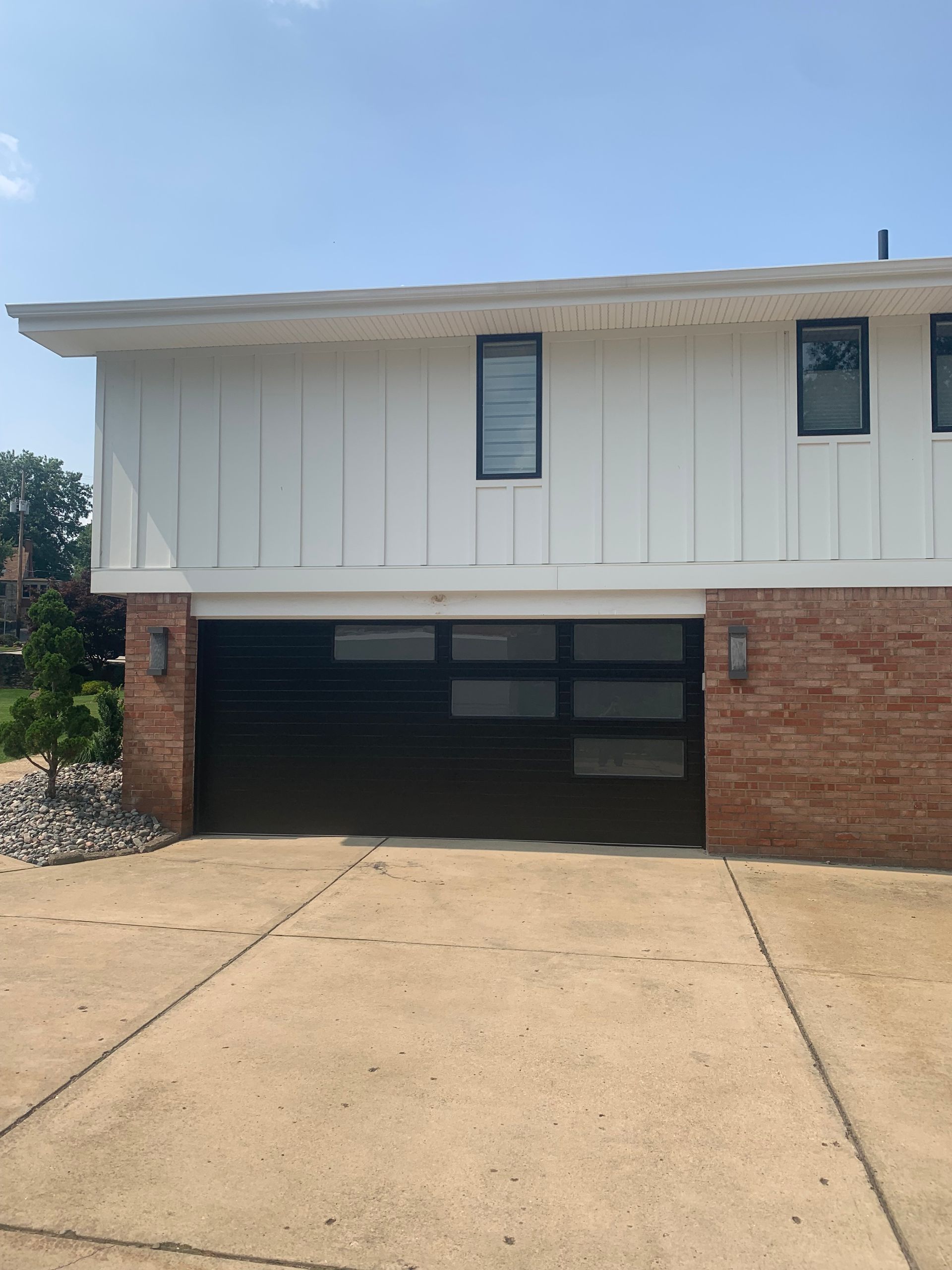 Black garage door with glass panels on a house with white siding and brick.