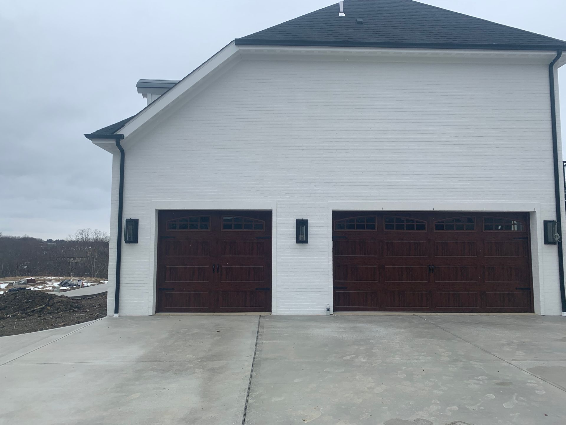 Two-car garage with brown doors and white siding on a concrete driveway. Gray sky in the background.