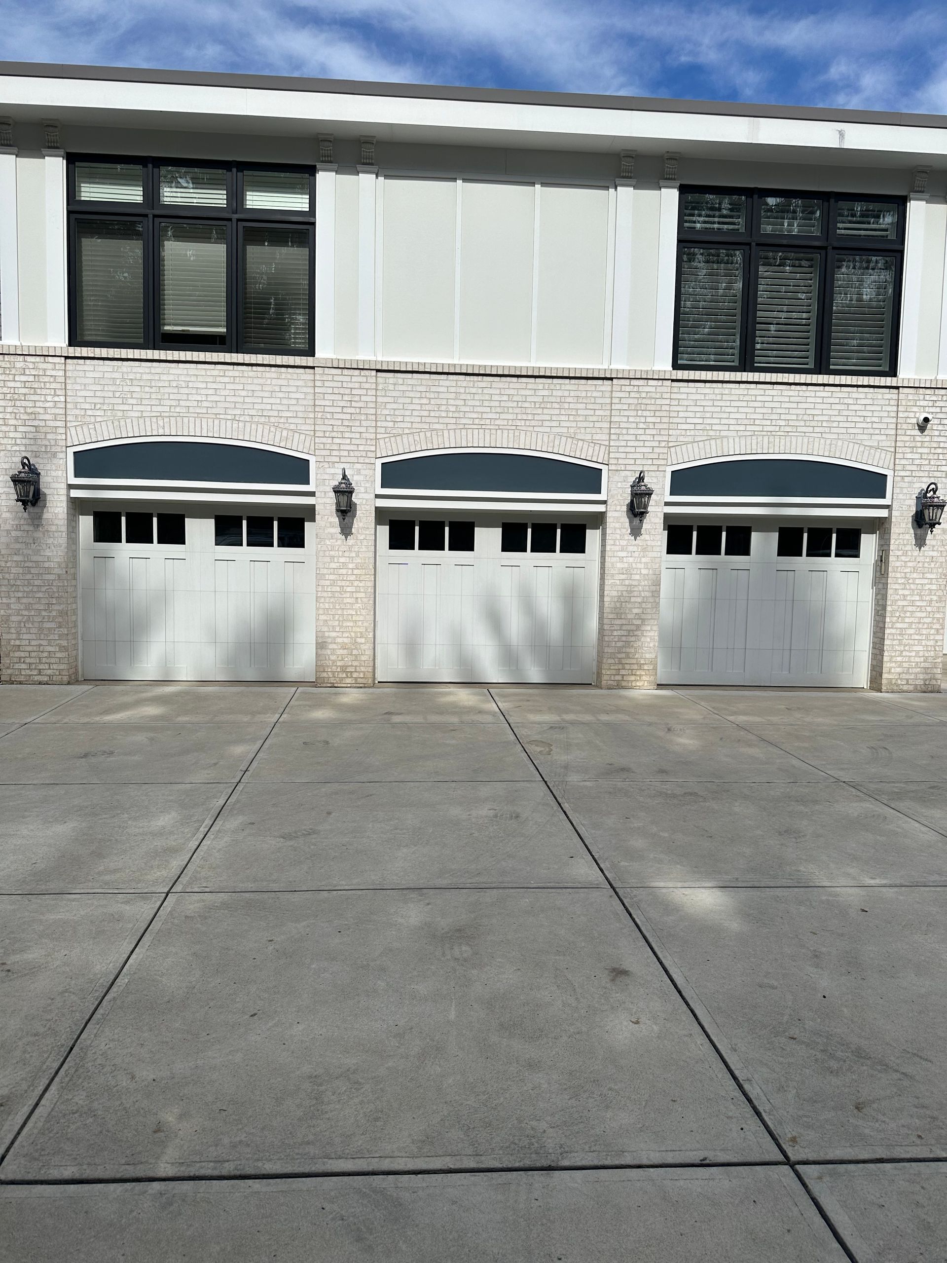 Three white garage doors with arched trim, set in a stone facade. Black-framed windows above.