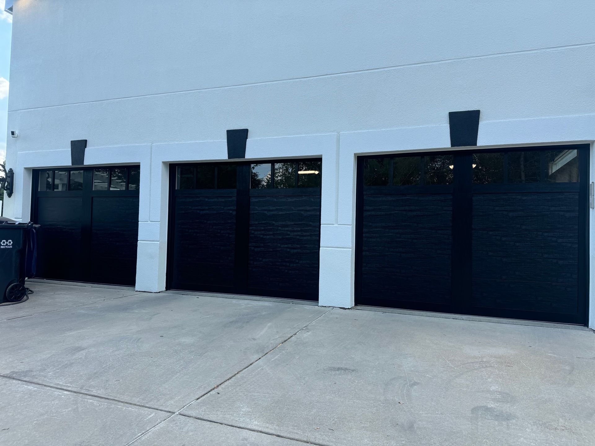 Three black garage doors with white trim on a white building.