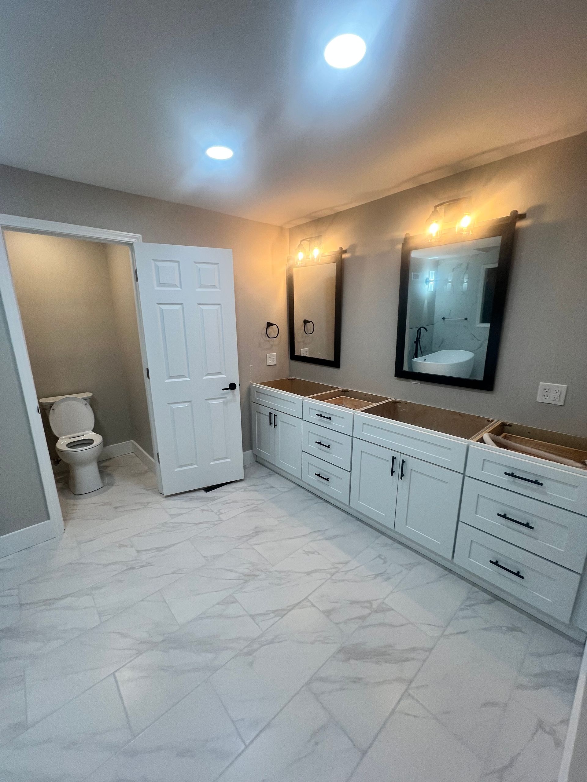 Bathroom with white cabinets, marble floor, two mirrors, and a toilet.