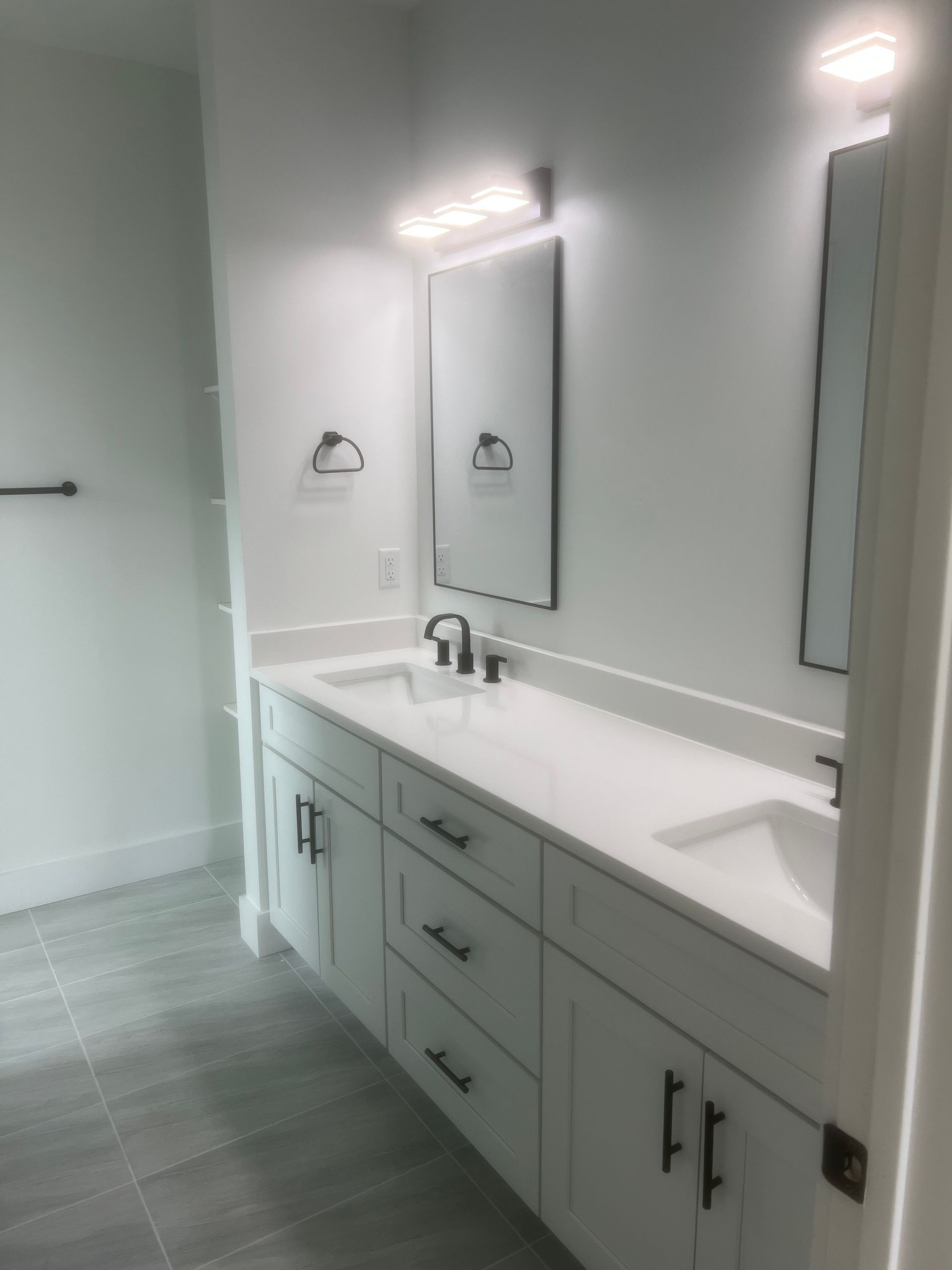 Modern white bathroom with double vanity, black hardware, and grey tile floor.