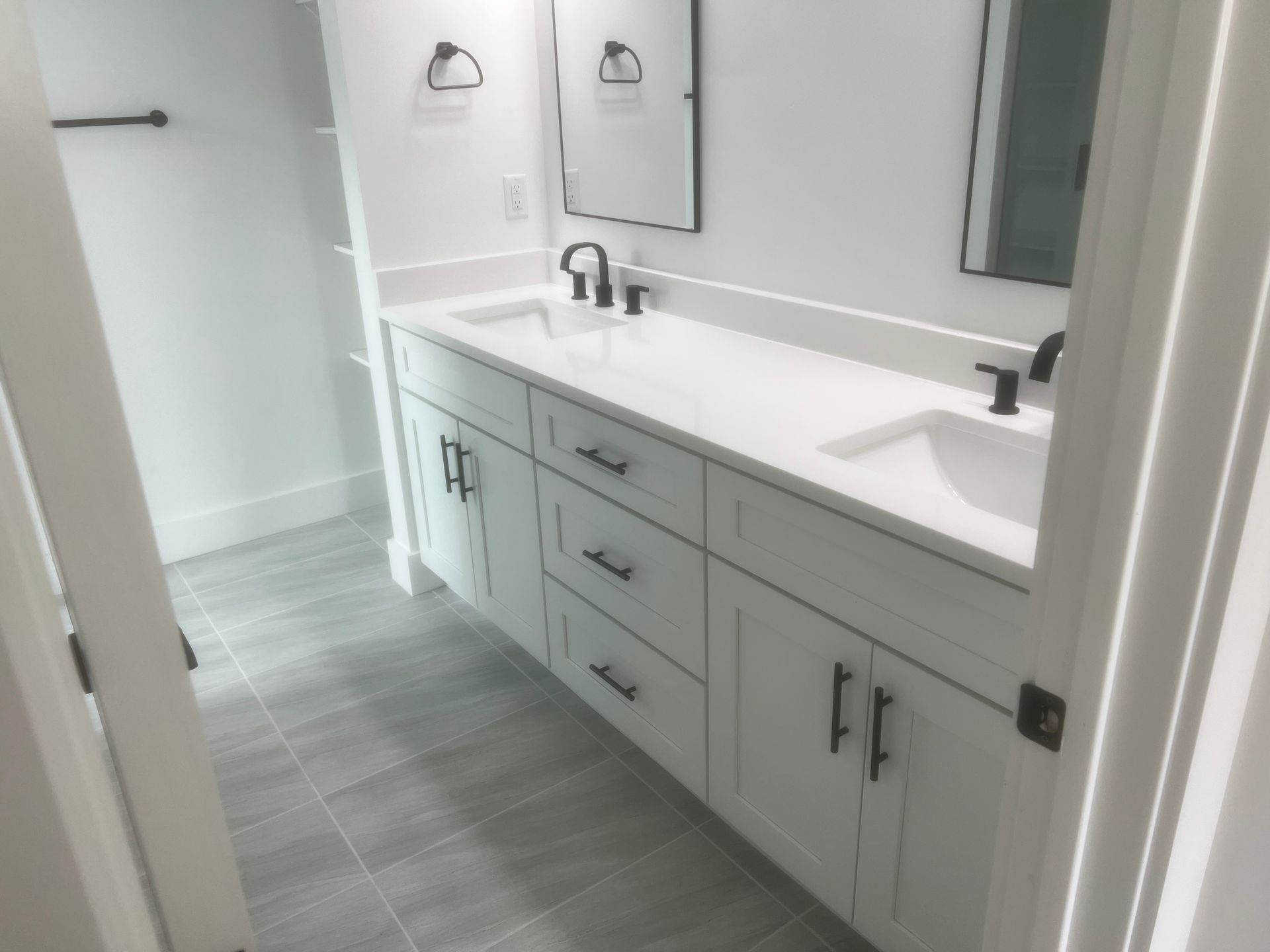 White bathroom vanity with black fixtures, two sinks, and a long countertop.