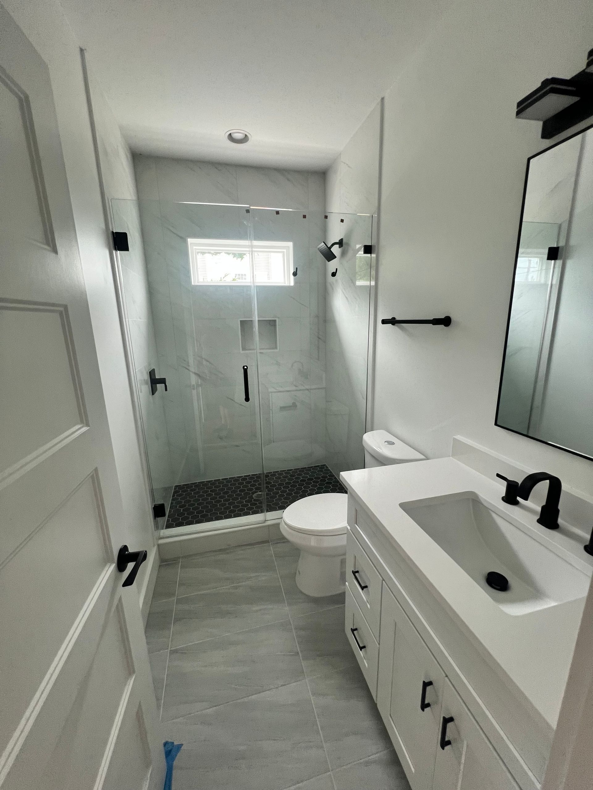 Small, modern bathroom with a glass shower, white vanity, and gray tile flooring.