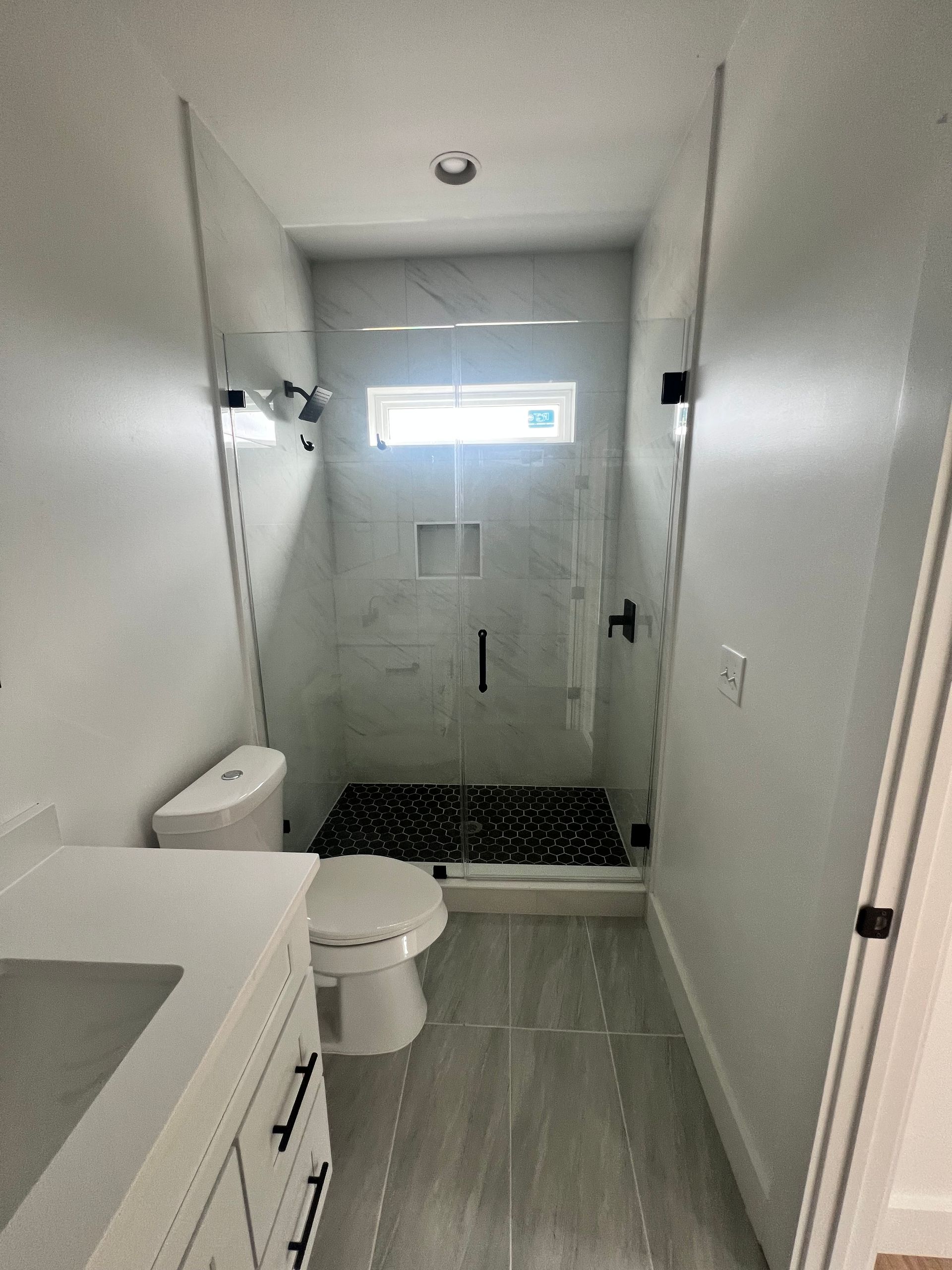 Narrow bathroom with shower, toilet, and vanity. Gray and white color scheme.