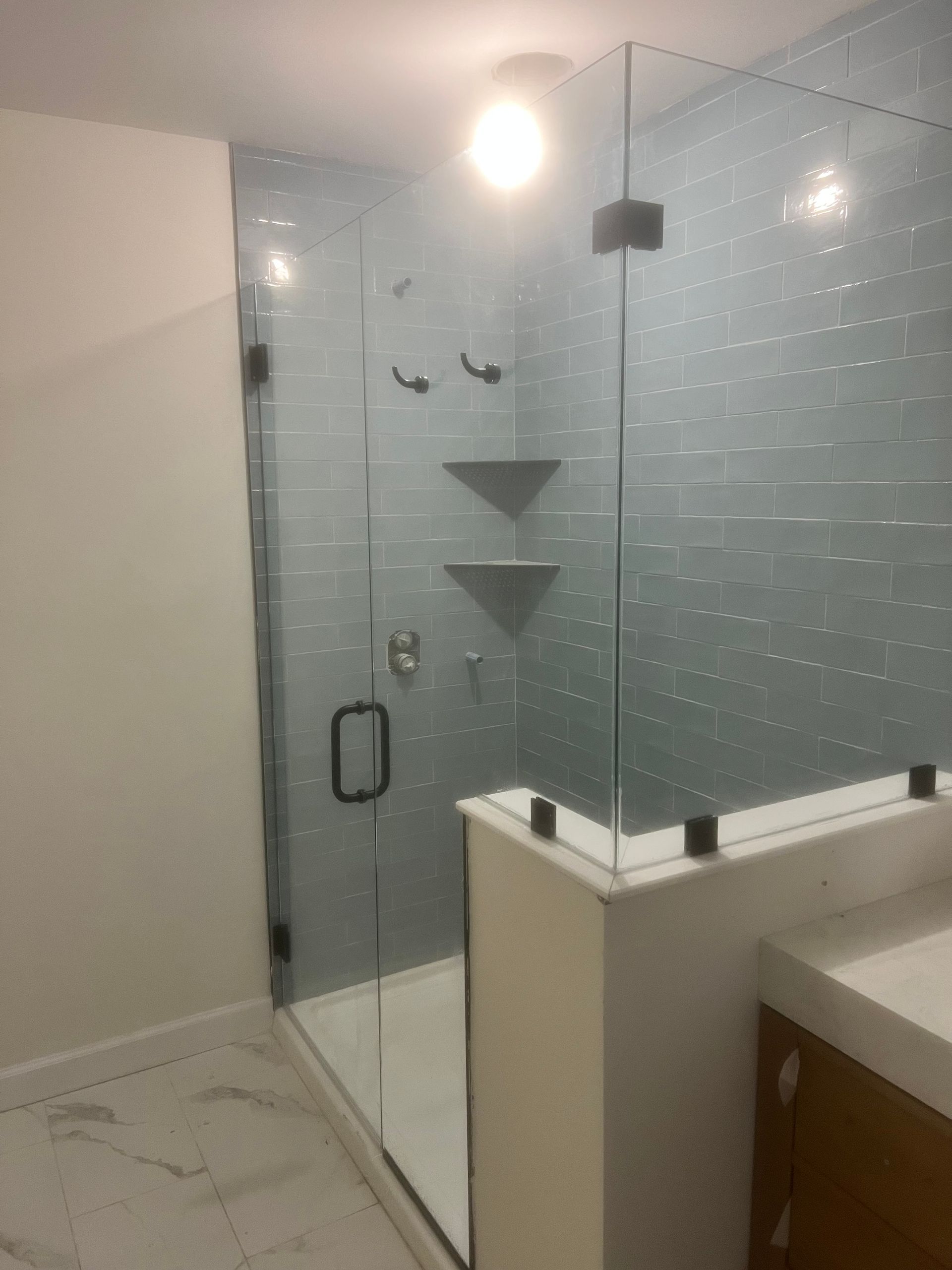 Glass shower enclosure with black hardware in a bathroom with blue tile and white walls.