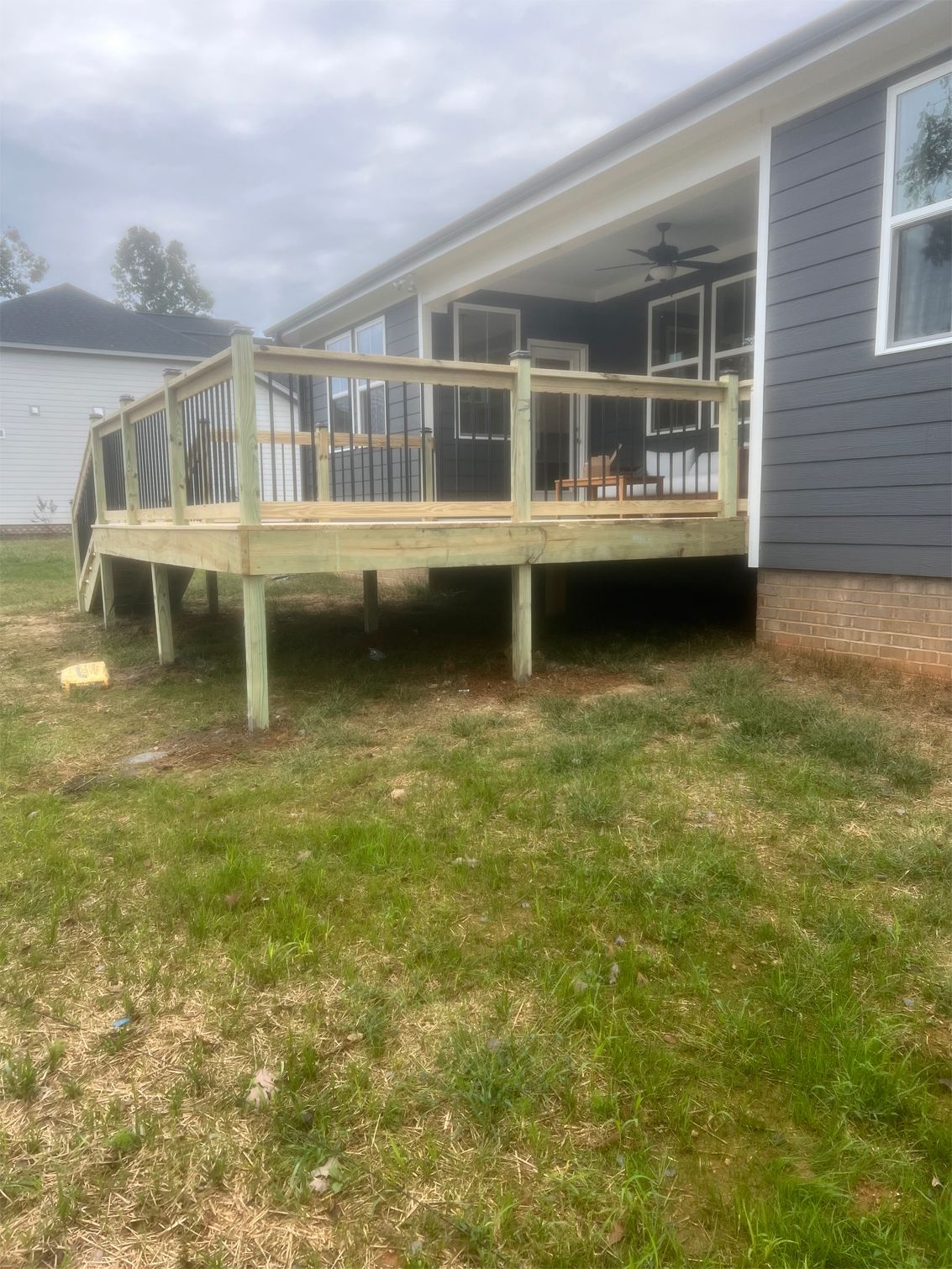 A wooden deck with railings is attached to a house with dark gray siding, set in a grassy yard.